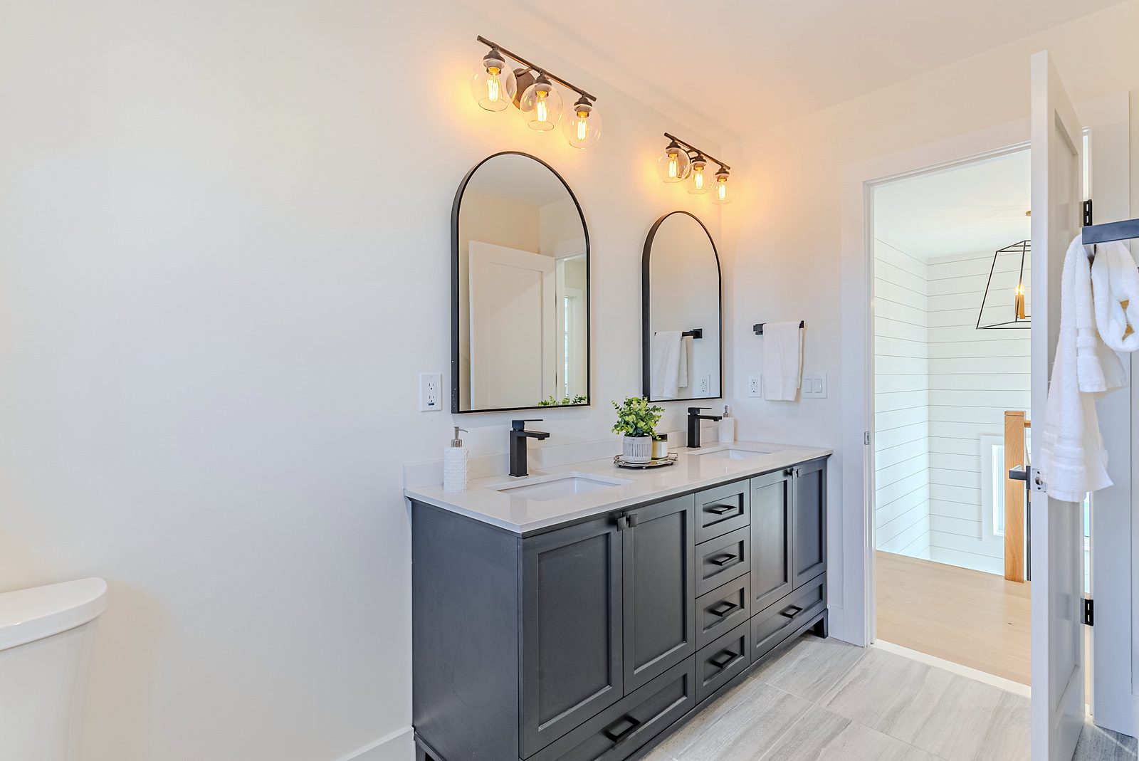 Primary bath: white-oak double vanity, black pulls and mirrors — White-oak and navy bathroom vanities with a freestanding tub and black fixtures