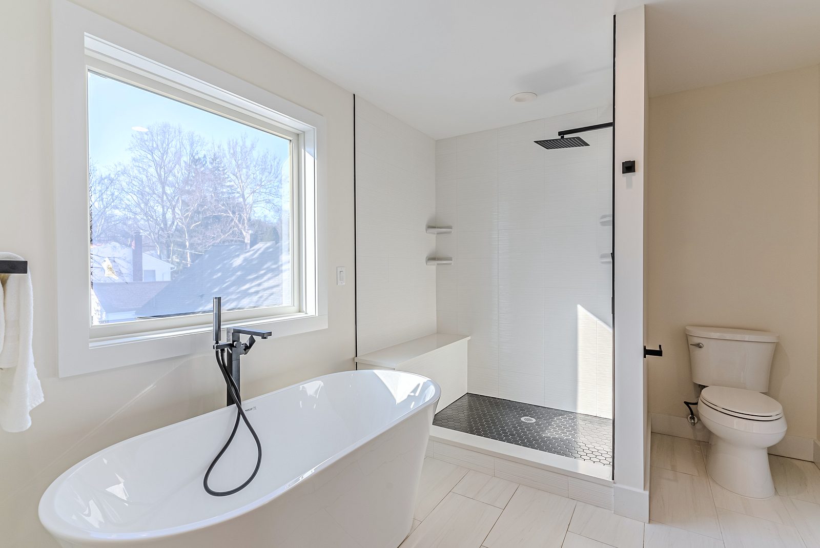 Freestanding tub with a black floor-mount filler, picture window — White-oak and navy bathroom vanities with a freestanding tub and black fixtures