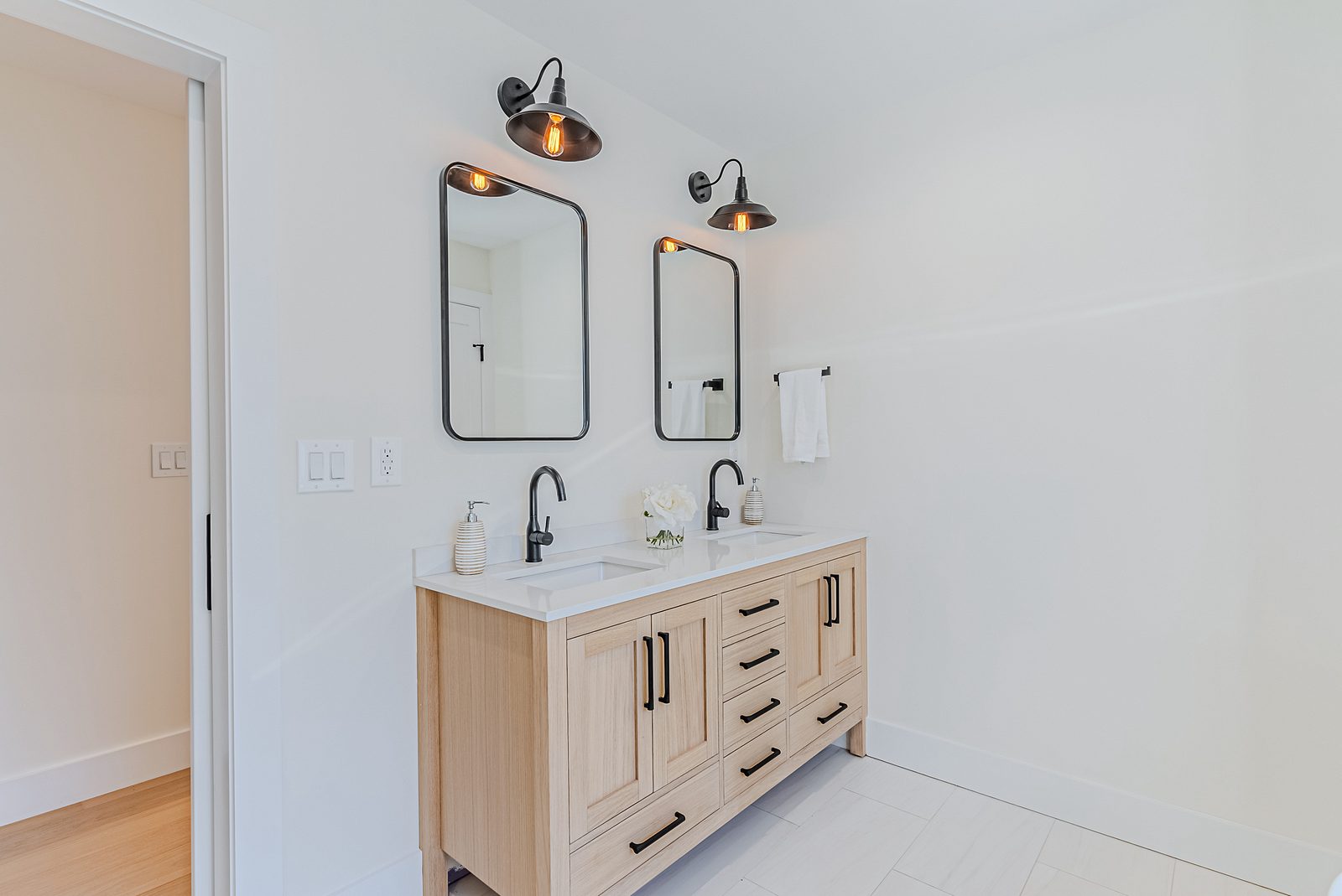 Walk-in shower with black fittings, bench and penny-tile floor — White-oak and navy bathroom vanities with a freestanding tub and black fixtures