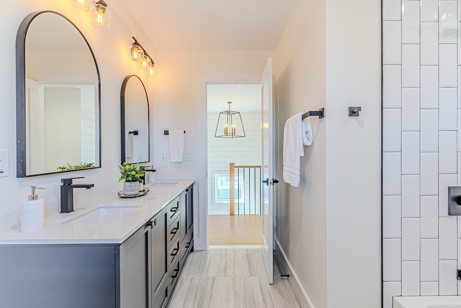 Second bath: navy double vanity, arched black mirrors, shiplap — White-oak and navy bathroom vanities with a freestanding tub and black fixtures