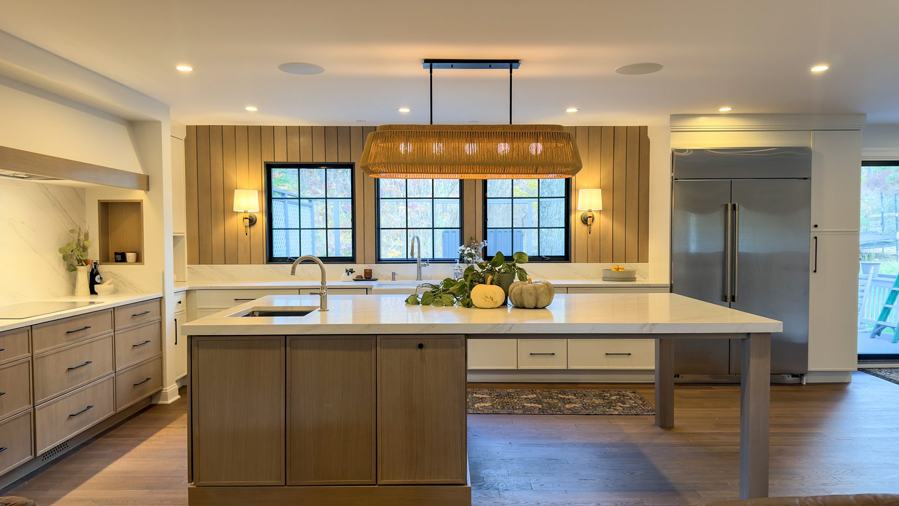Cream kitchen with a white-oak island, a wood-slat window wall, black-framed windows and a rattan linear pendant