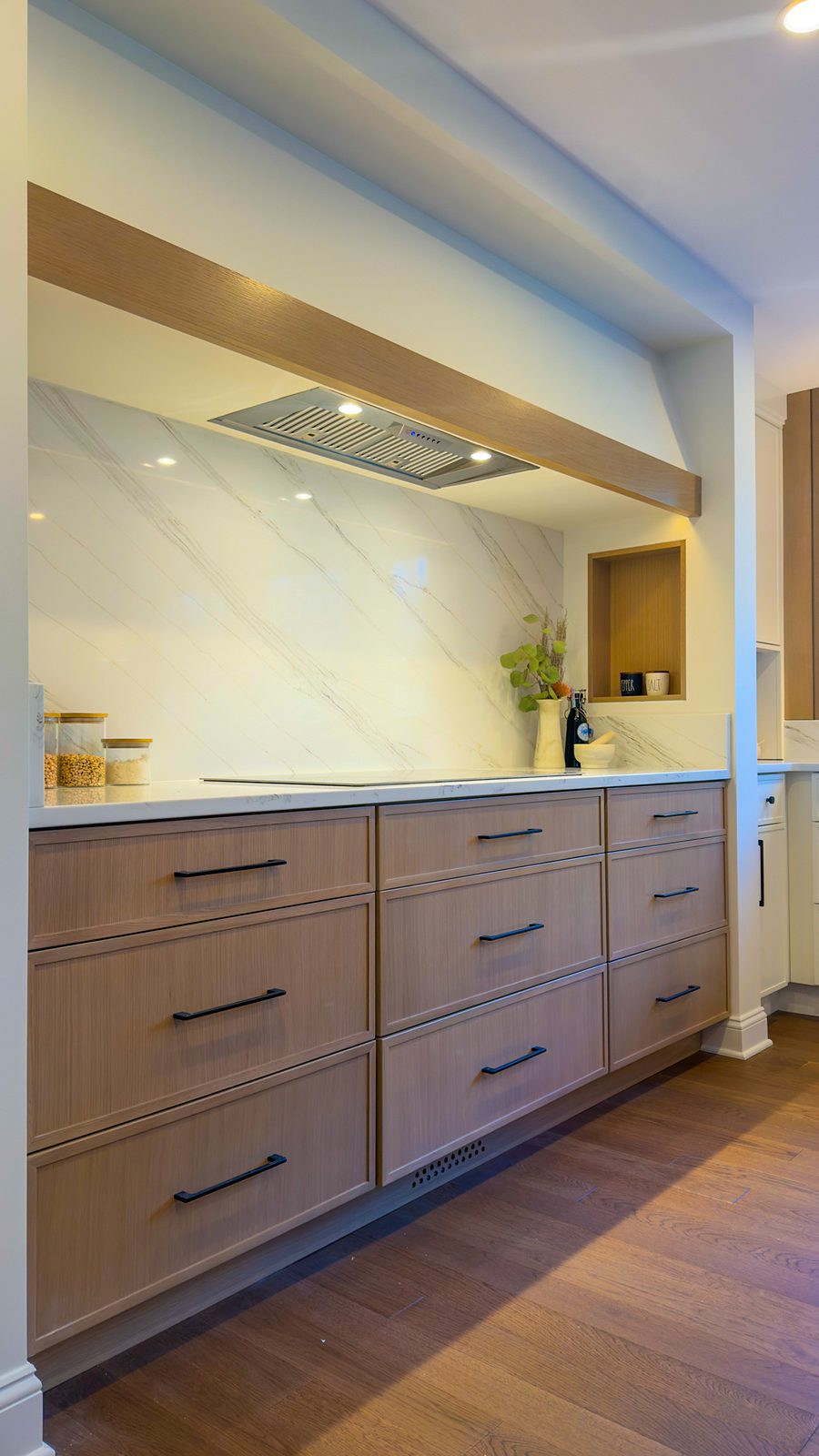 Cooking alcove lined in a marble-look slab under an oak beam, with white-oak base cabinets