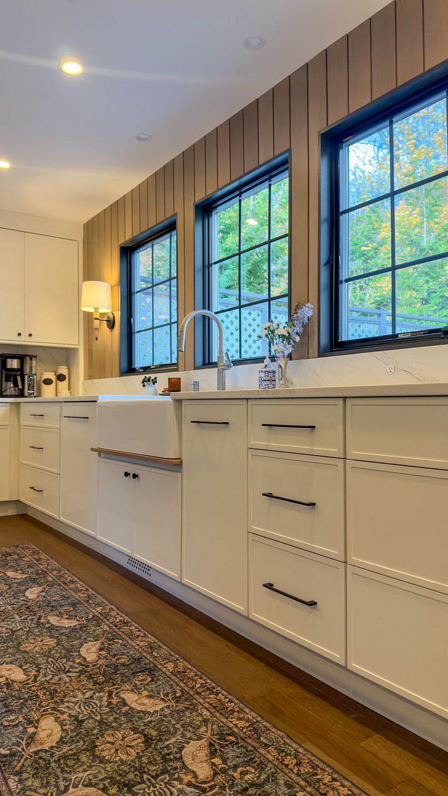 Sink wall with the apron-front sink, cream cabinets and black-framed windows in the slat wall