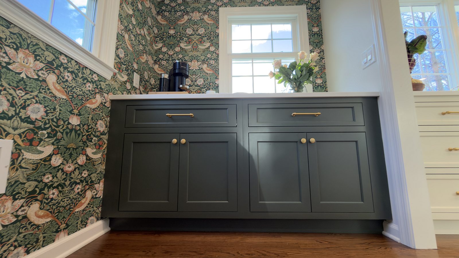 Green buffet with brass knobs set into the floral wallpaper