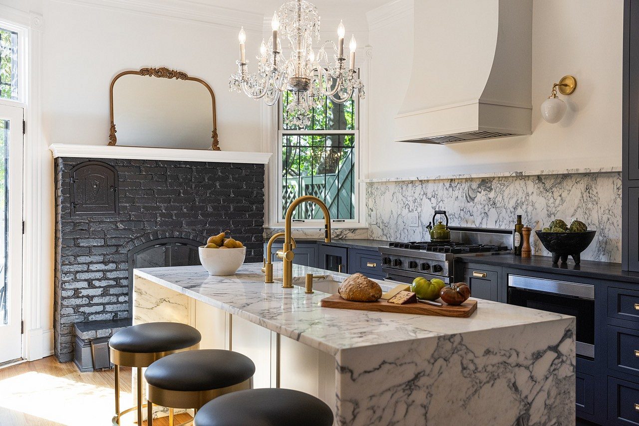 Hale Navy inset kitchen with a white island under a veined marble waterfall top, a black-painted brick fireplace and a crystal chandelier