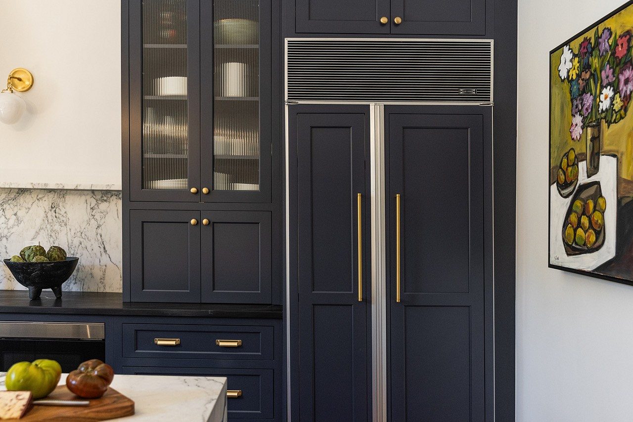 Navy hutch with reeded-glass uppers beside the panel-ready refrigerator with brass pulls