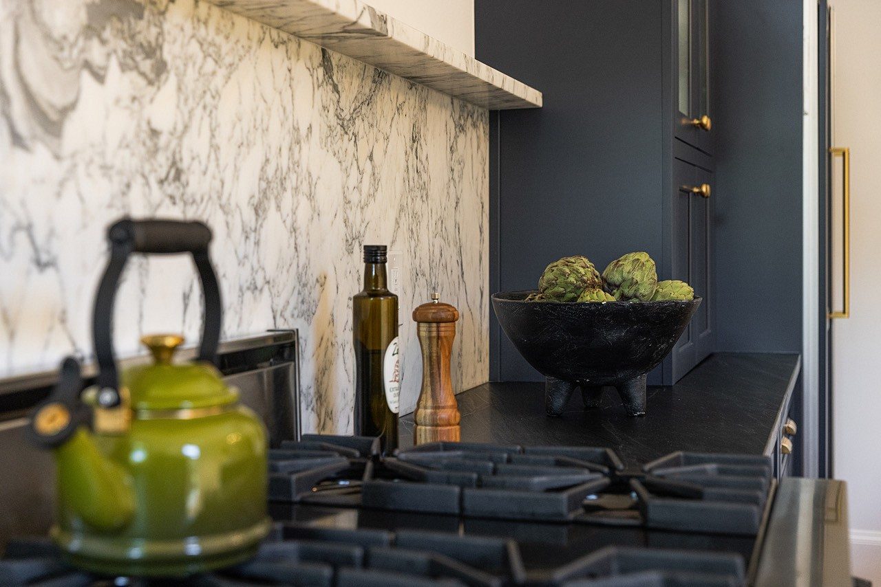 Range wall: full-height marble slab backsplash with a ledge, matte black counters and navy cabinets