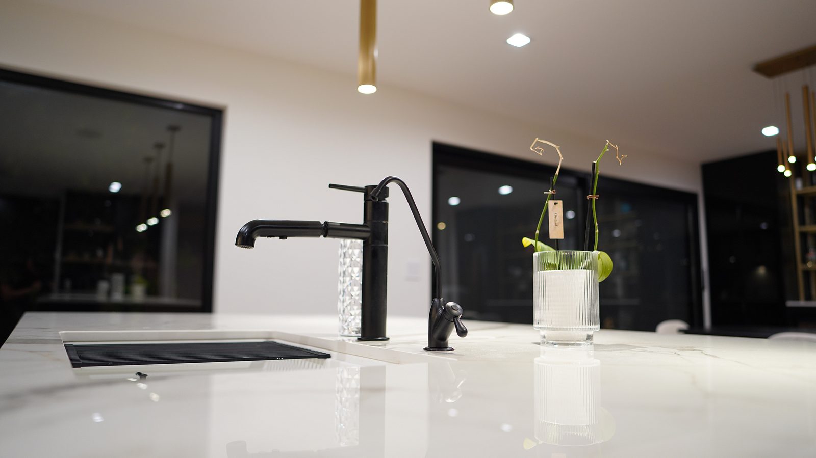 Matte black faucet on the marble-look island top with black-framed windows behind
