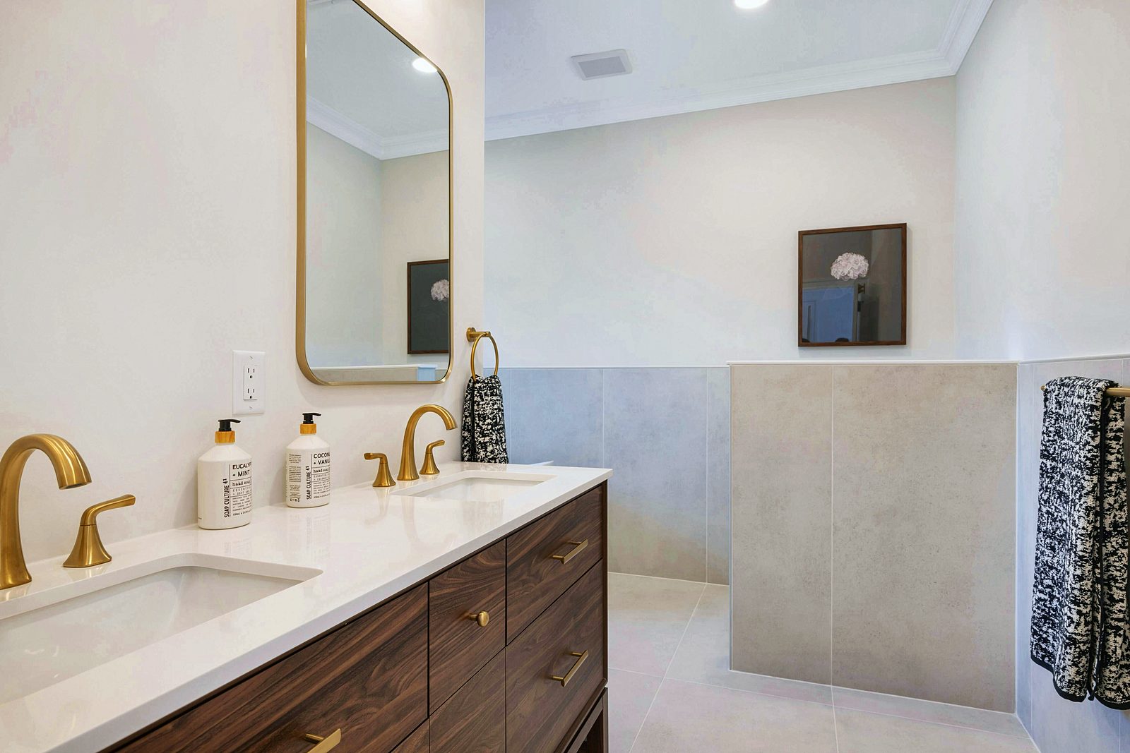 Walnut double vanity under a brass-framed mirror