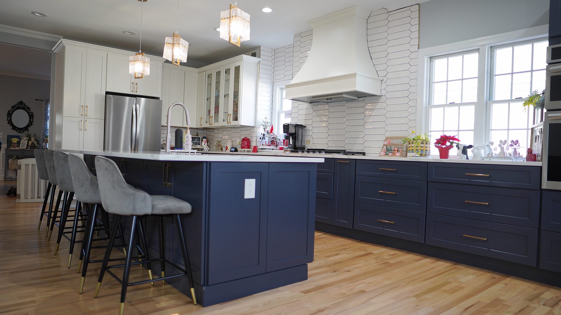 Navy and white shaker kitchen with a navy island, crystal pendants, a white custom hood and a picket-tile backsplash