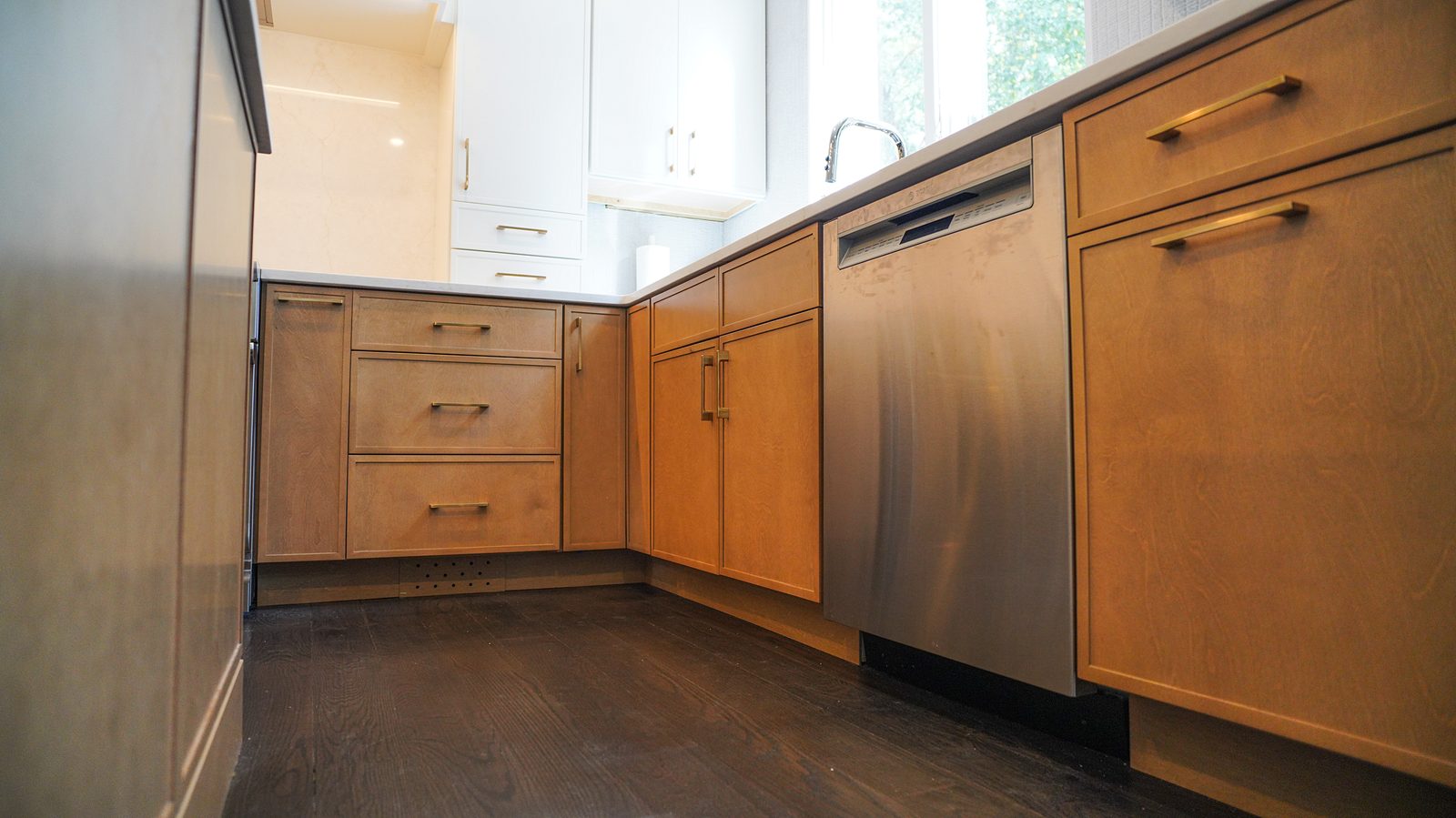 Oak base cabinets with slim brass pulls beside the built-in refrigerator