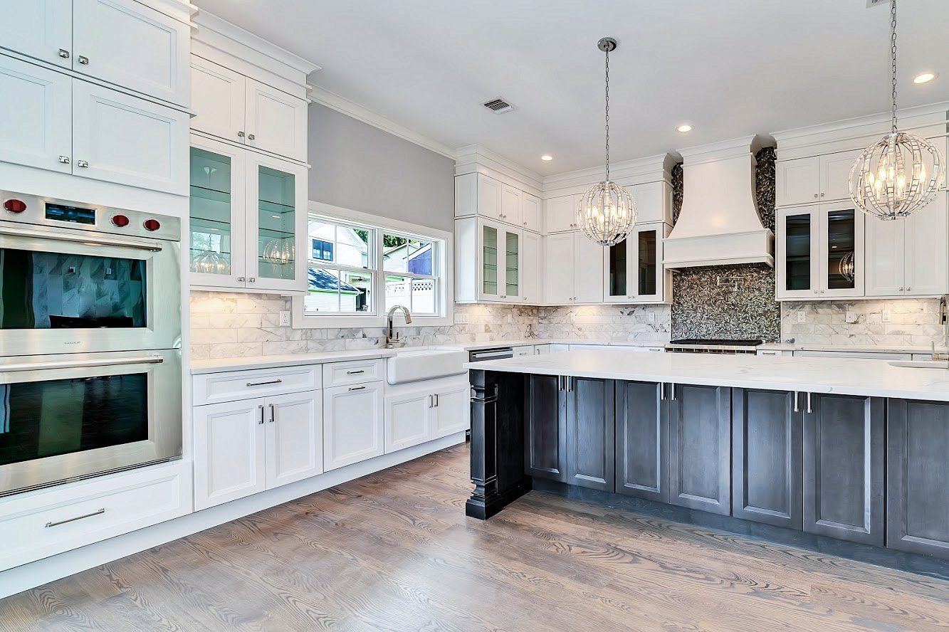 White shaker perimeter with glass-front uppers — White shaker kitchen with a long charcoal island in a two-story great room