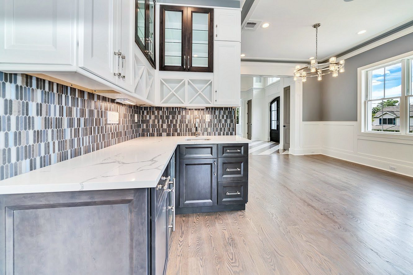Bar with a gray-and-white tile backsplash — White shaker kitchen with a long charcoal island in a two-story great room