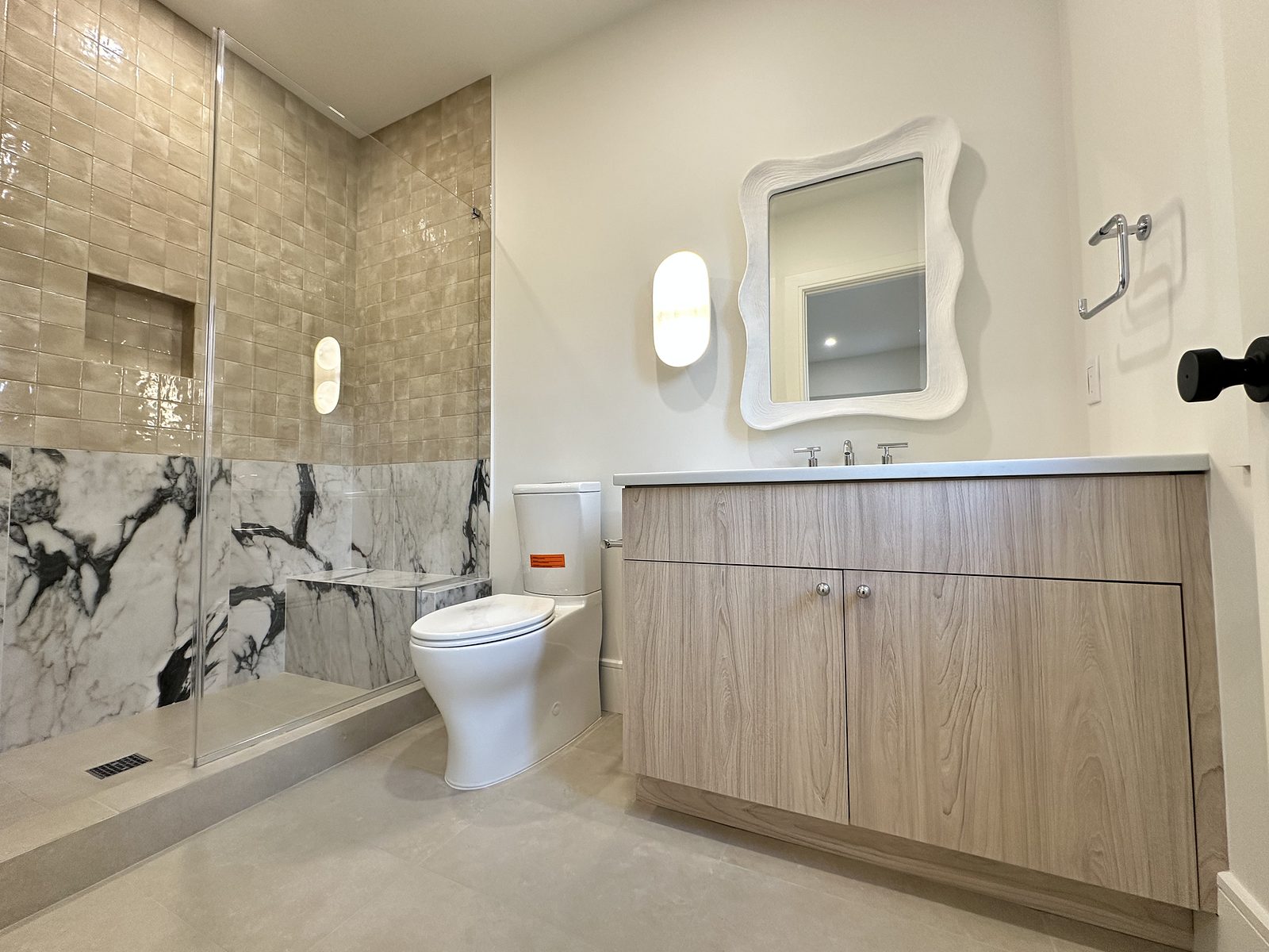 Second bath with a wood-grain vanity, a curved mirror and a marble-look shower
