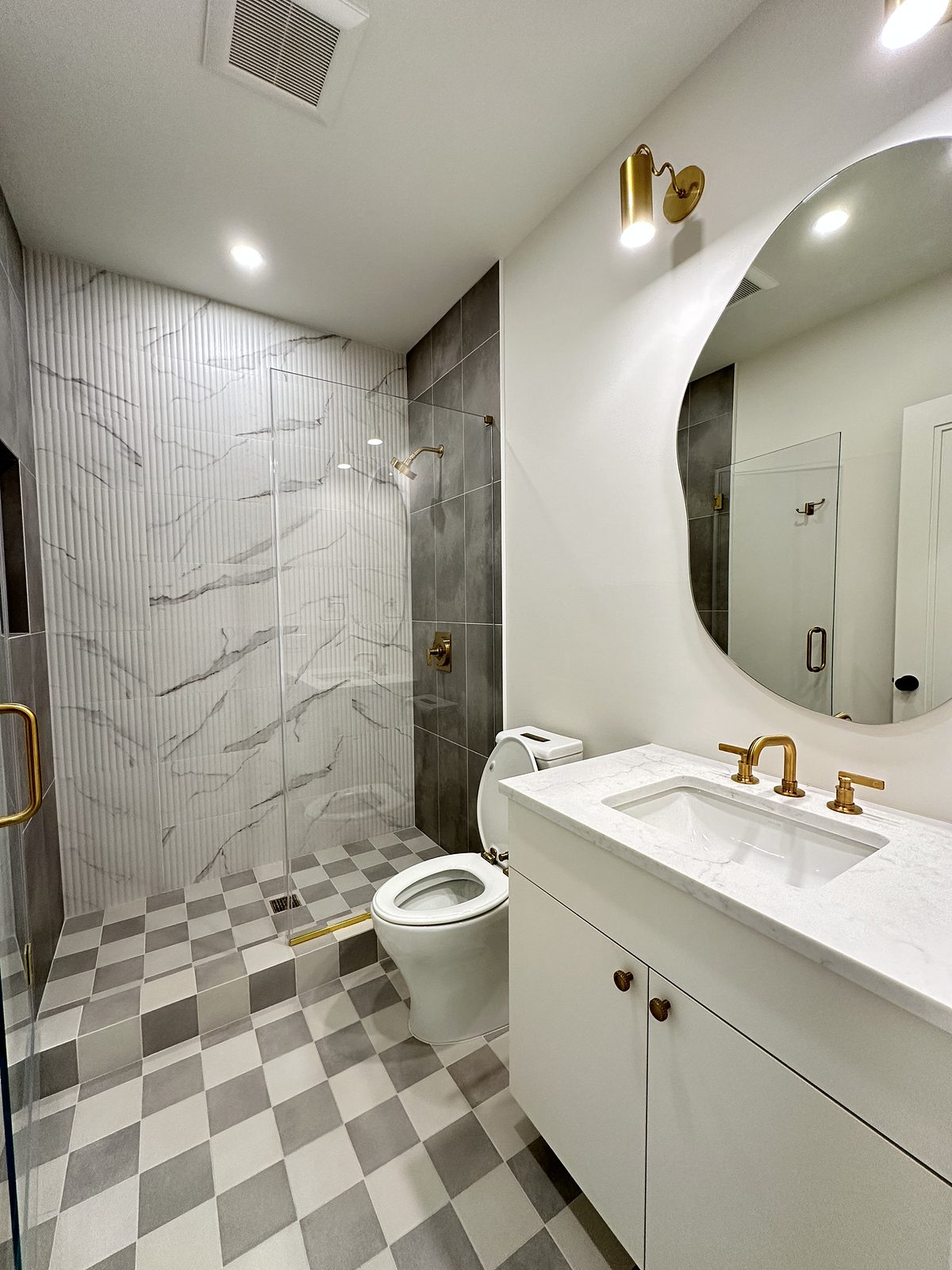 Third bath: white slab vanity with a brass faucet, marble-look shower and checkerboard floor