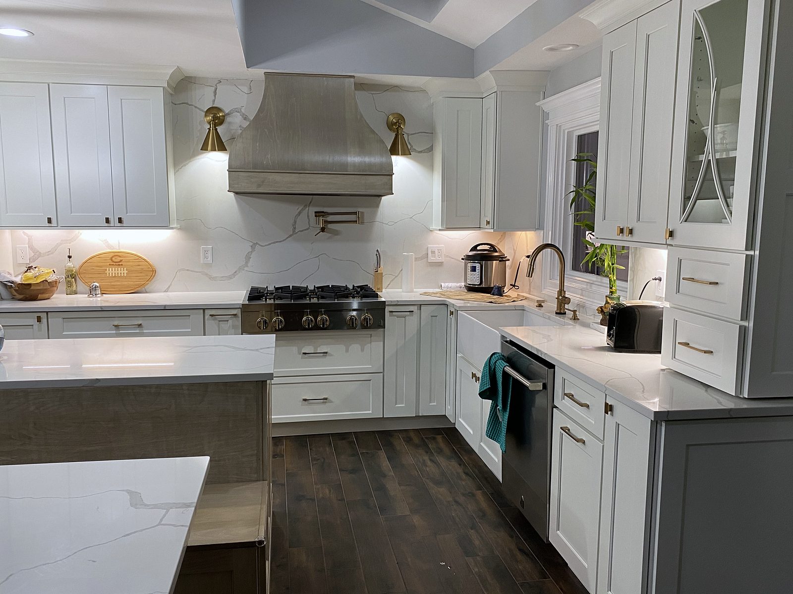 Glass-front uppers, pro-style range, built-in refrigerator — Shiloh Heritage kitchen in Polar and Seagull with a bench island and a gray wood hood