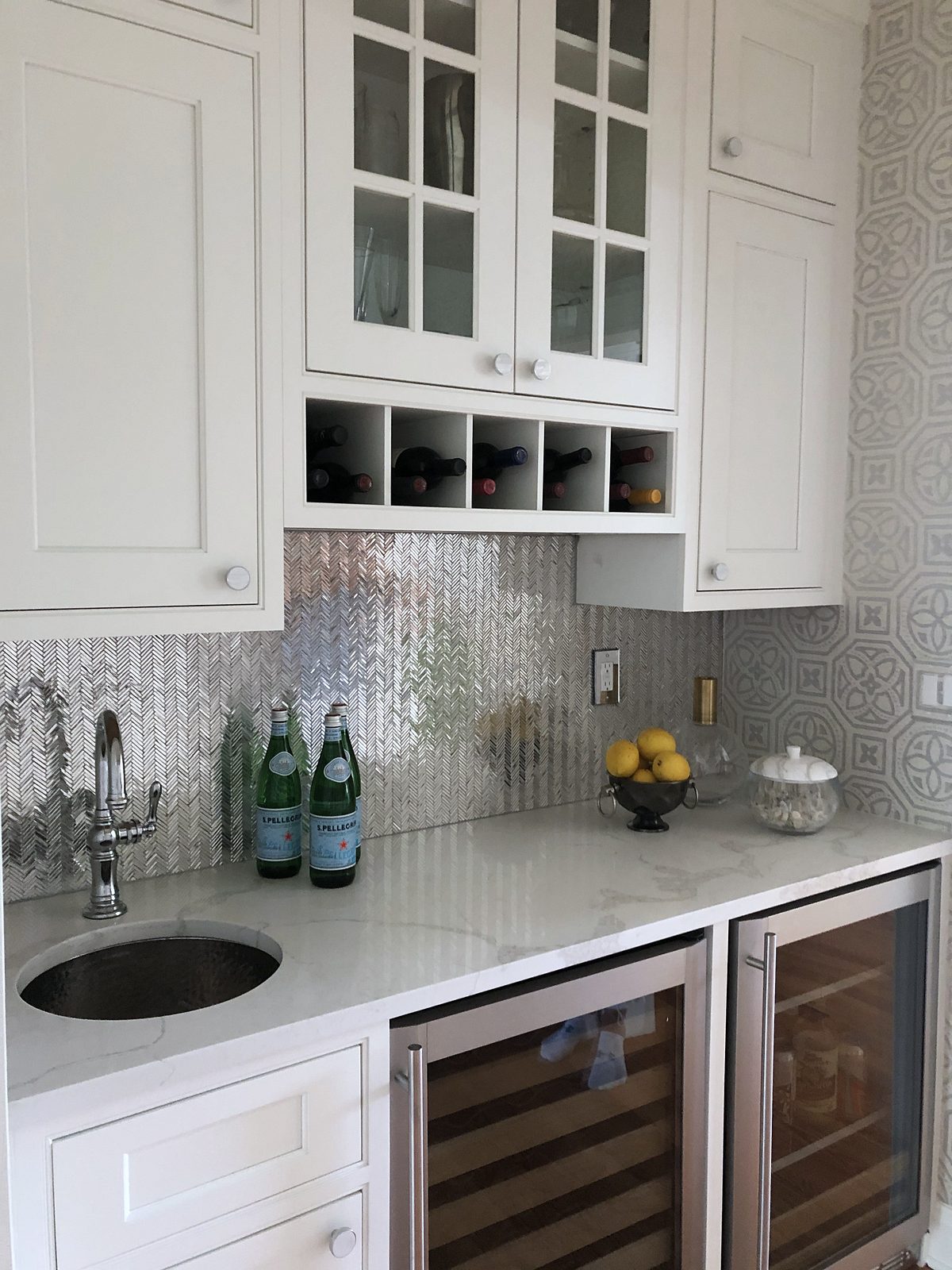 Butler’s pantry in the same white door with wine cubbies, a beverage fridge and a metallic penny-round backsplash