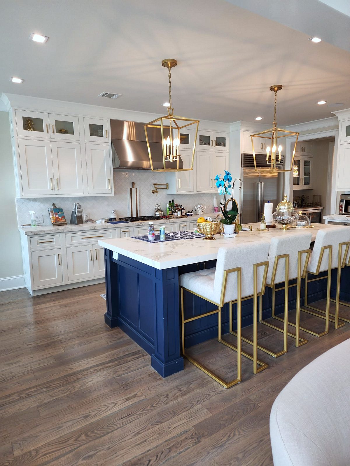 Navy island with brass pulls and gold-framed stools — Shiloh inset kitchen with stacked white uppers and a navy island