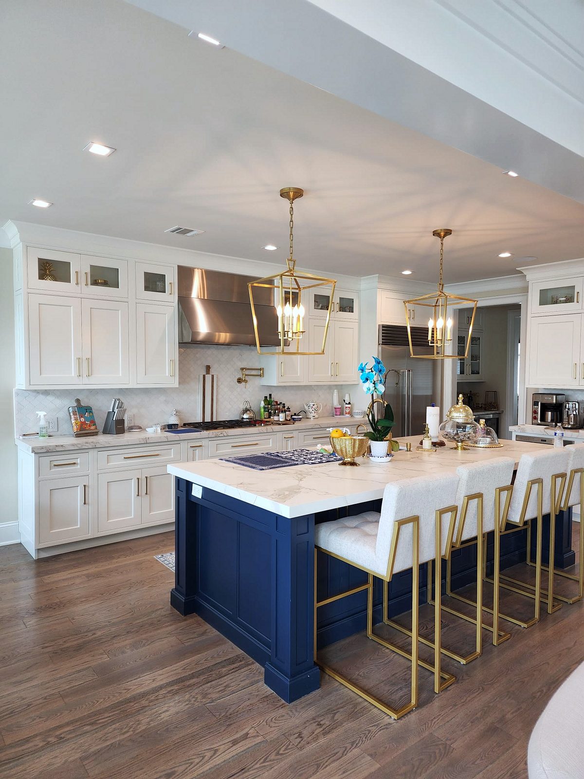 Marble-look slab, stainless chimney hood, pro-style range — Shiloh inset kitchen with stacked white uppers and a navy island