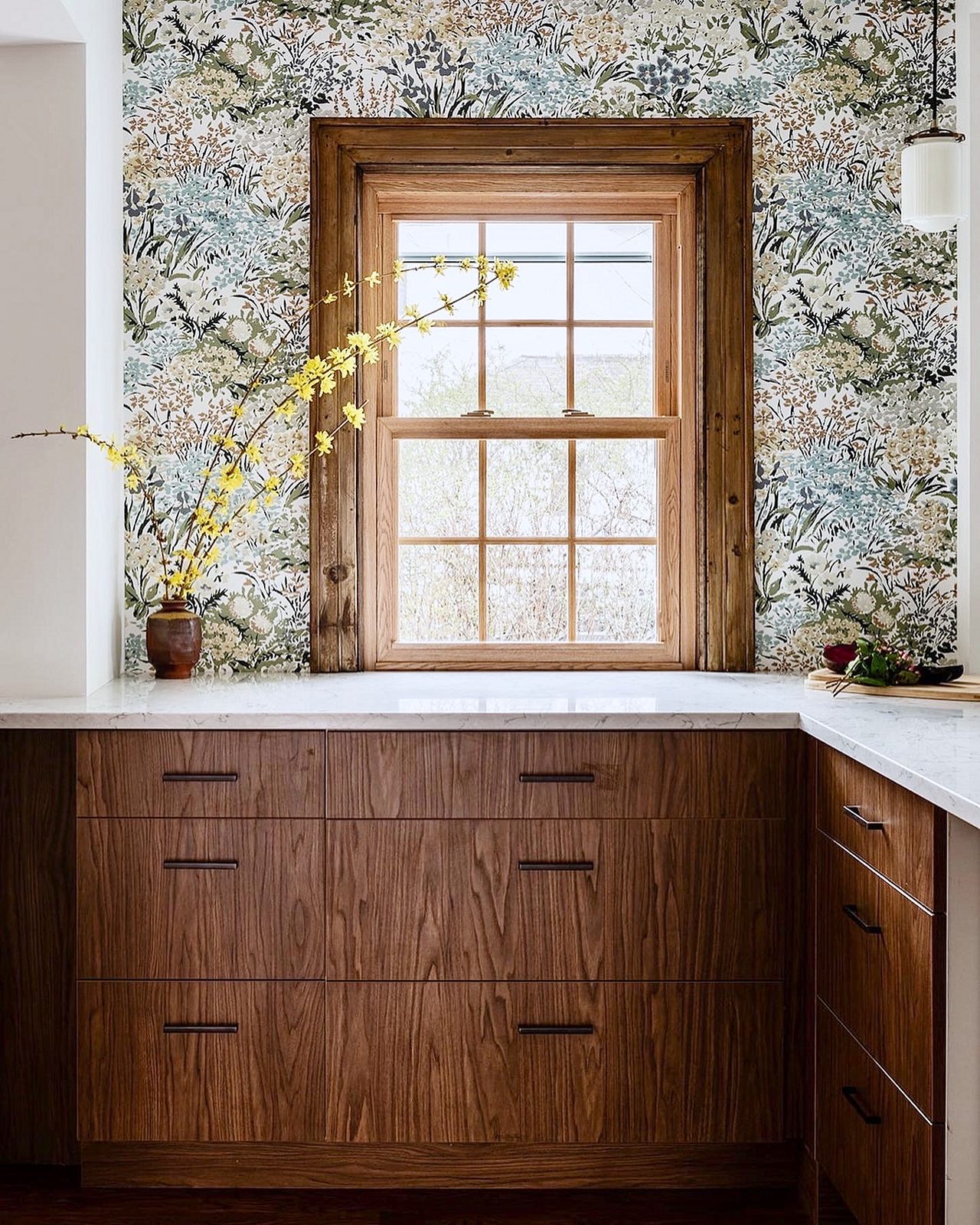 Farmhouse sink with a brass bridge faucet; brass-bracket shelves — Walnut slab kitchen with marble-look quartz, a farmhouse sink and brass