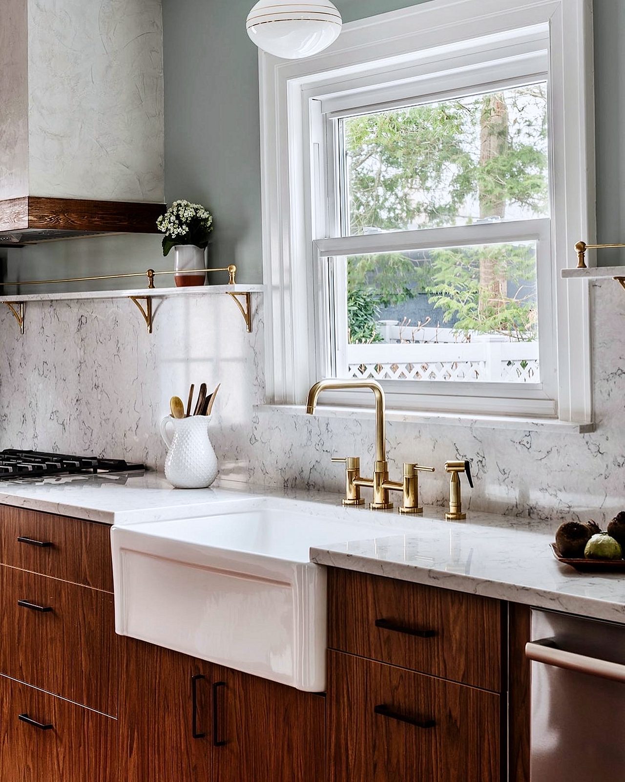 Plaster-look hood with a walnut band over a stainless range — Walnut slab kitchen with marble-look quartz, a farmhouse sink and brass