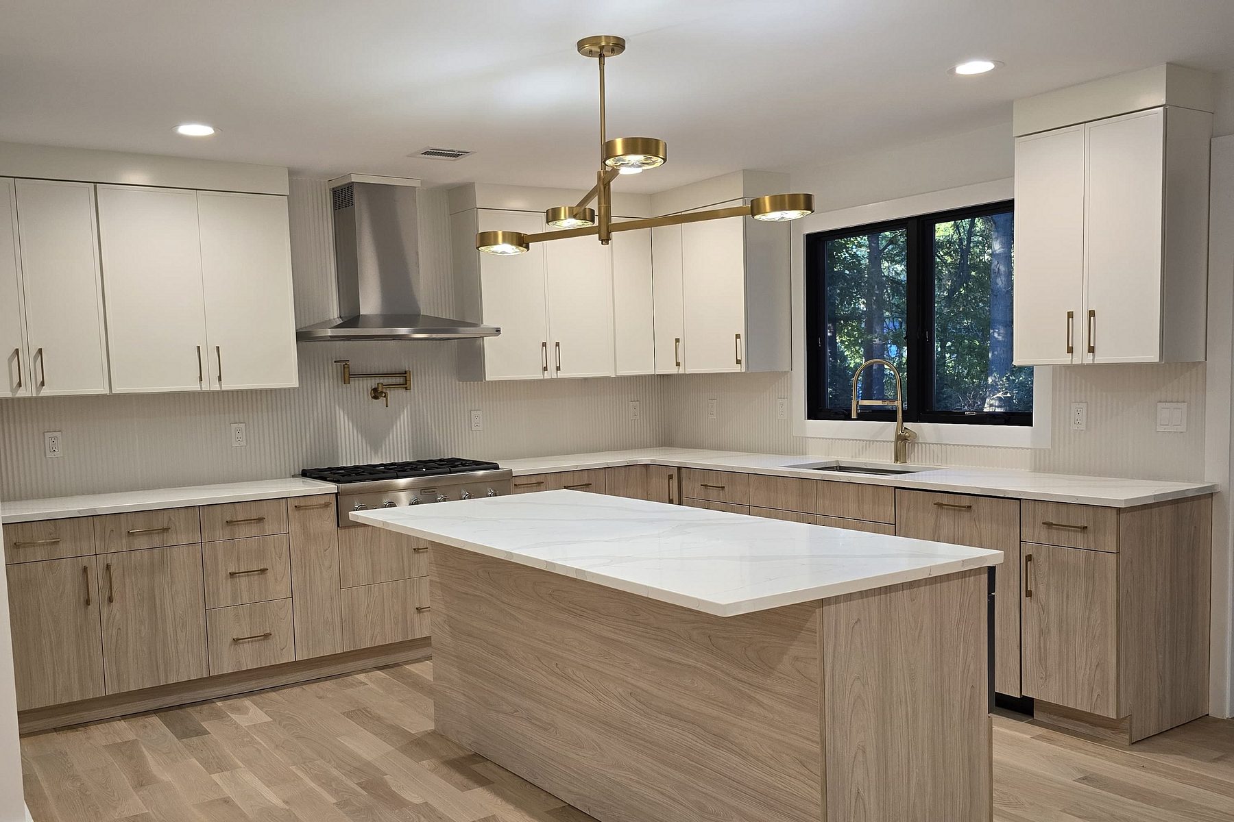 White and driftwood flat-panel kitchen with a marble-look quartz island, a brass linear chandelier and a stainless chimney hood