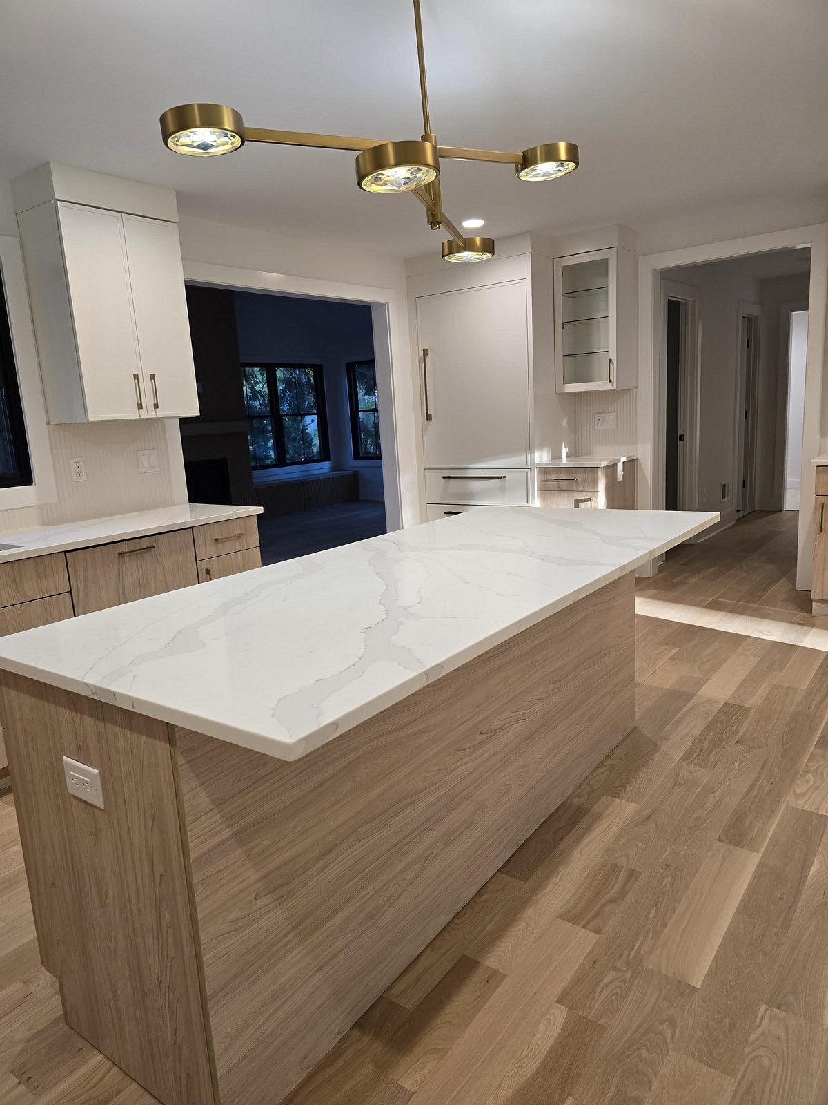 The island under the brass chandelier with the white tall cabinets behind