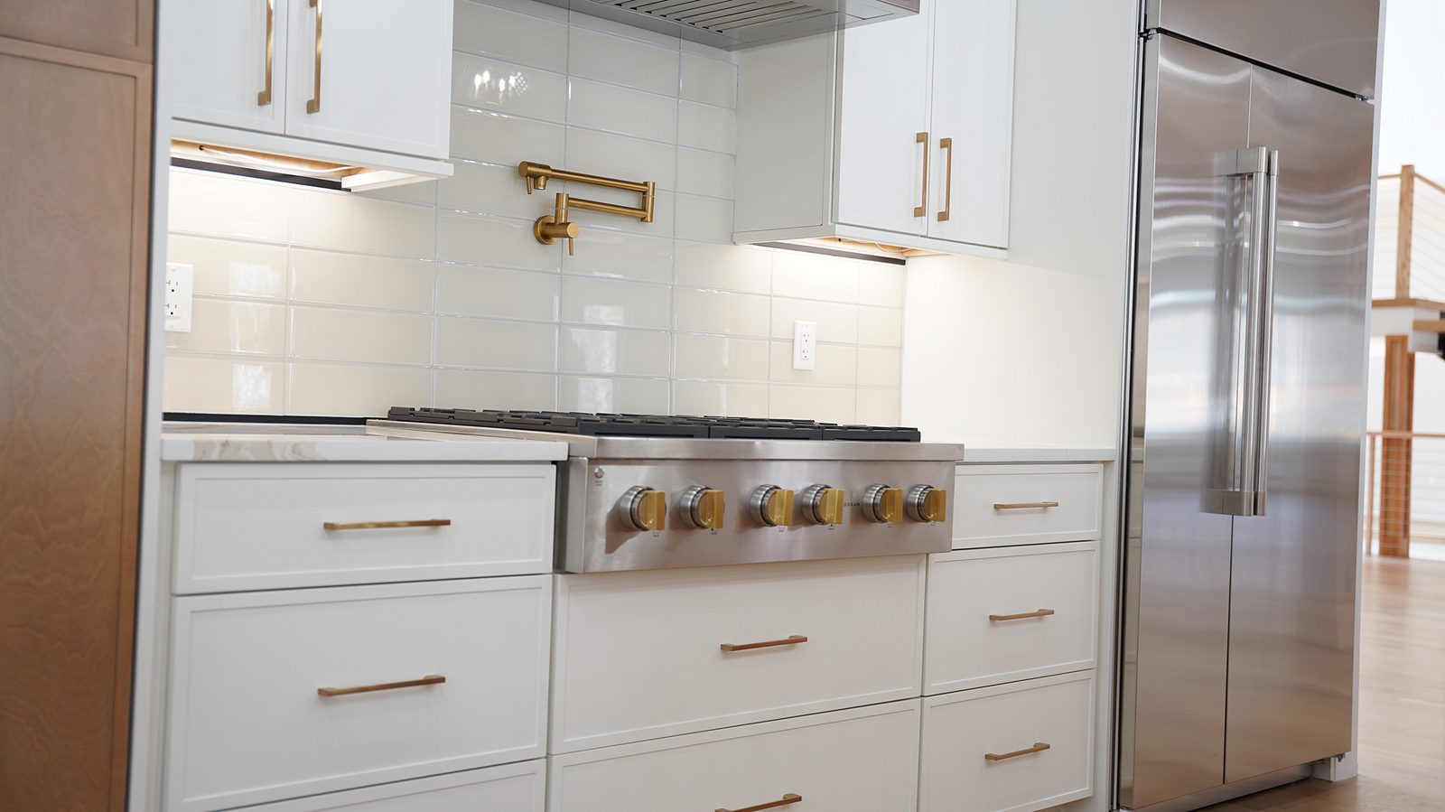 Pro-style cooktop under a stainless chimney hood beside the built-in refrigerator