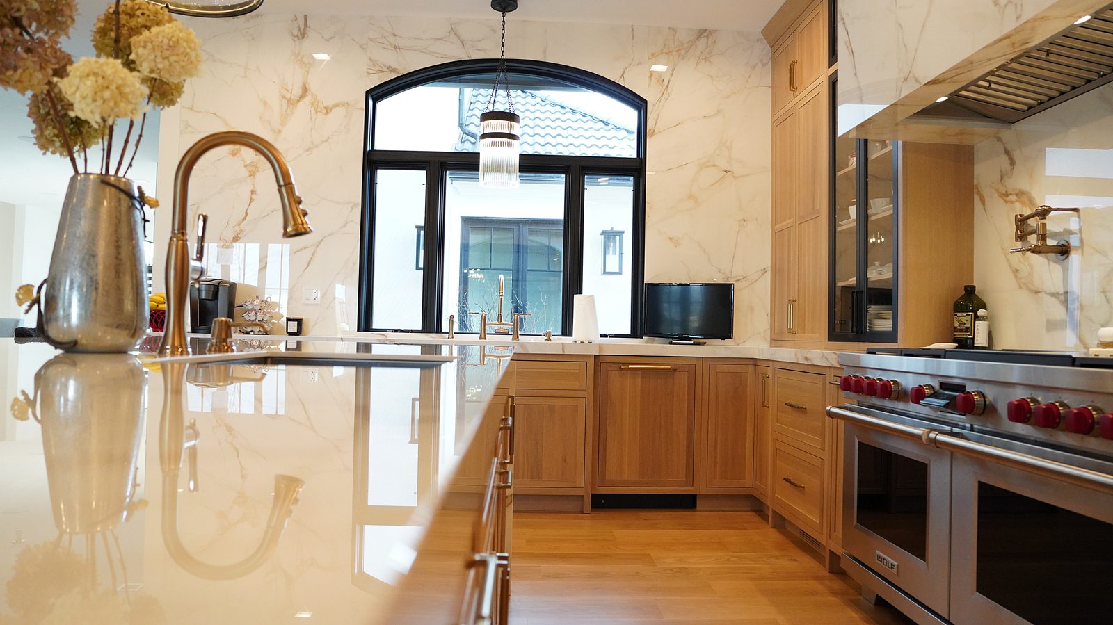 Sink under the arched window with the full-height Calacatta-look backsplash and pro-style range