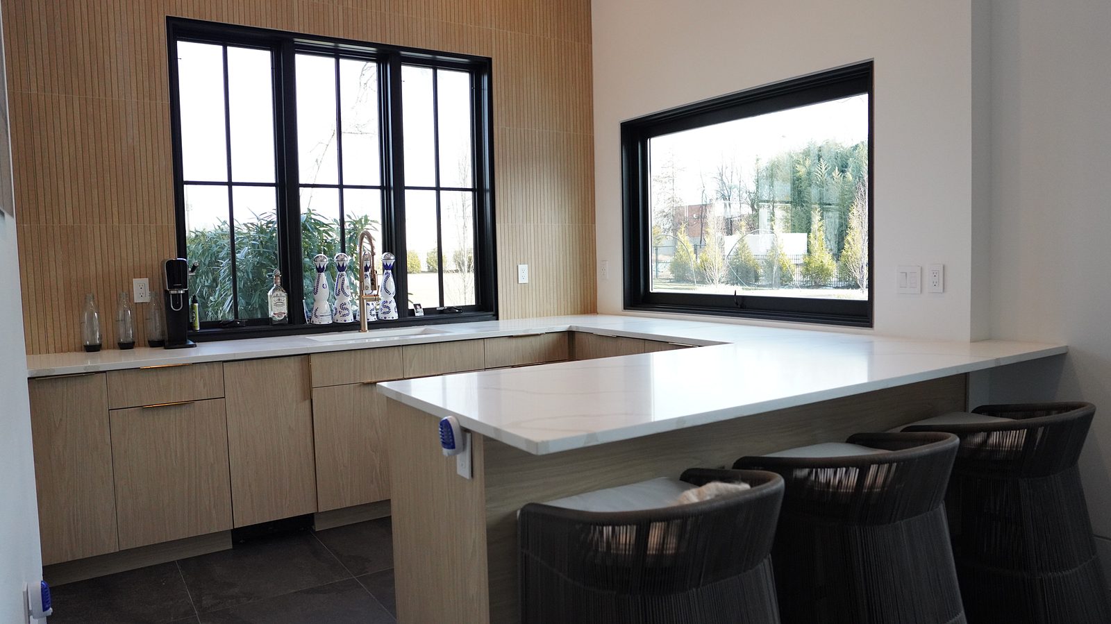 Oak bar counter under black-framed windows with black-and-brass stools