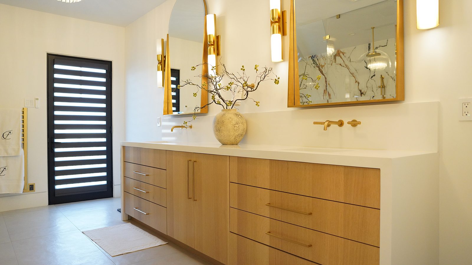 White-oak double vanity with brass wall-mounted faucets, brass-framed mirrors and sconces
