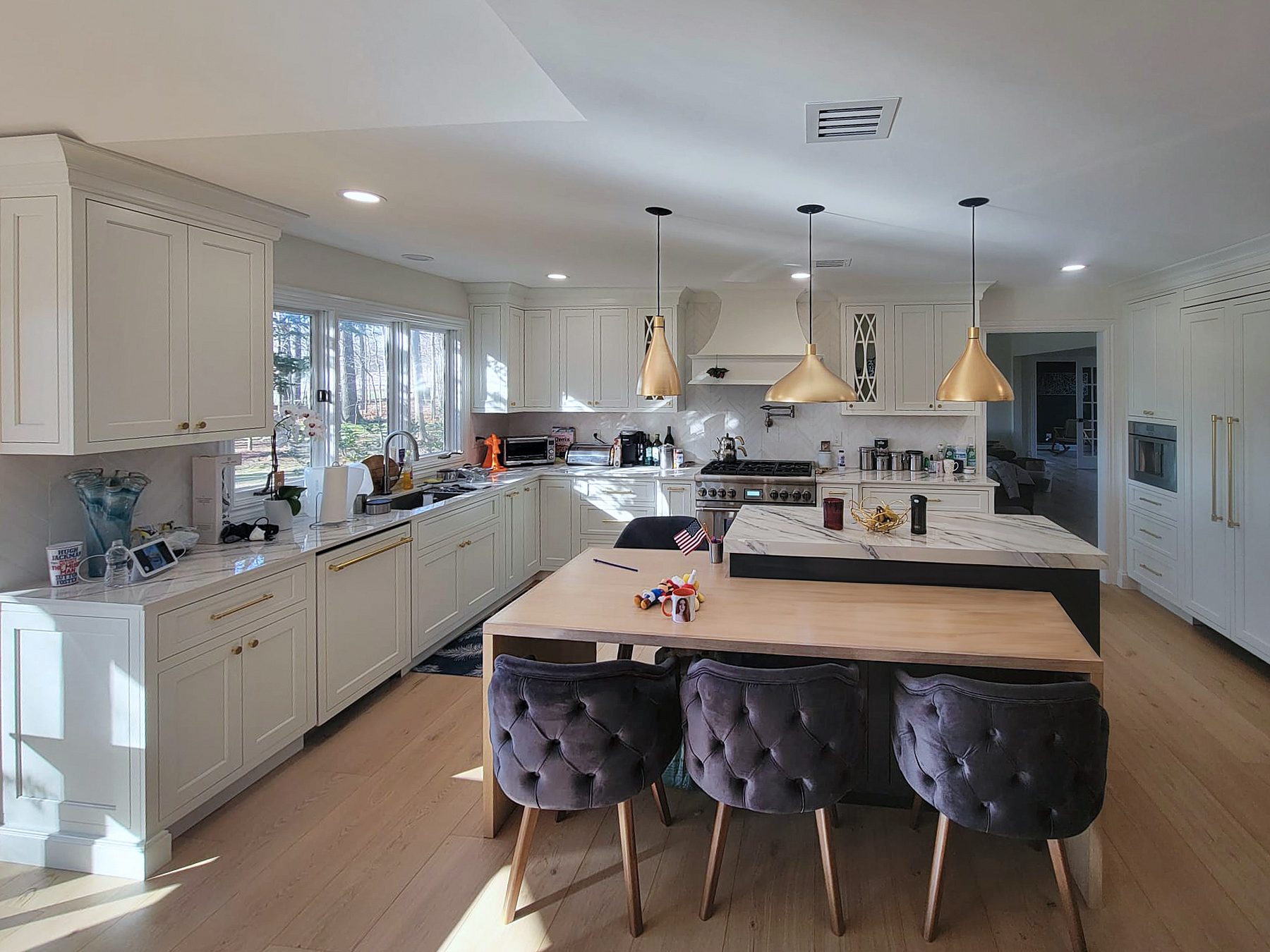 White Shiloh kitchen in Polar with a navy Hudson island under a Dekton Trance top, brass pendants and a wood table extension