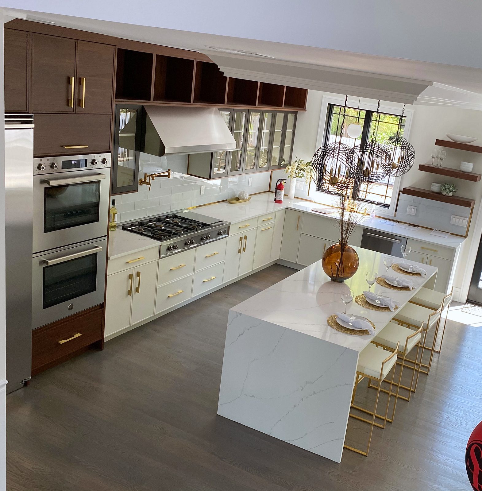 Gold bar pulls, glass globe pendants — White slab and walnut kitchen with a waterfall island