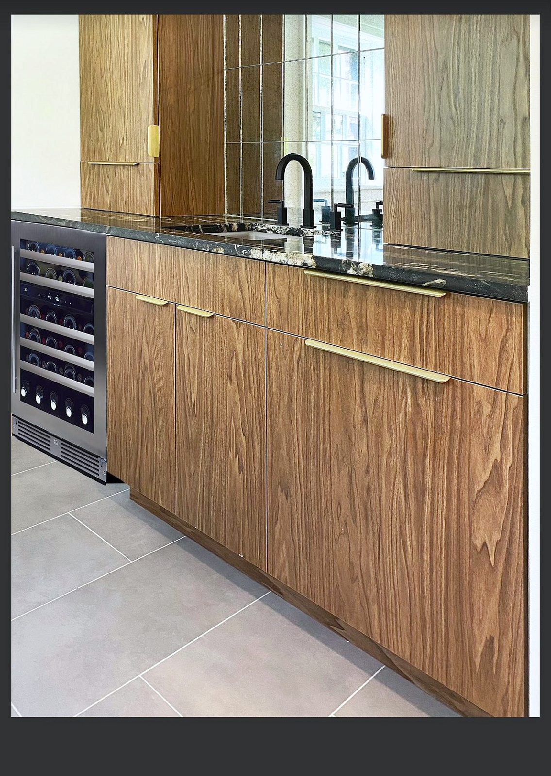 Farmhouse sink with a brass faucet; pro-style range — Wood-grain slab kitchen with brass pulls and a mirrored wine bar