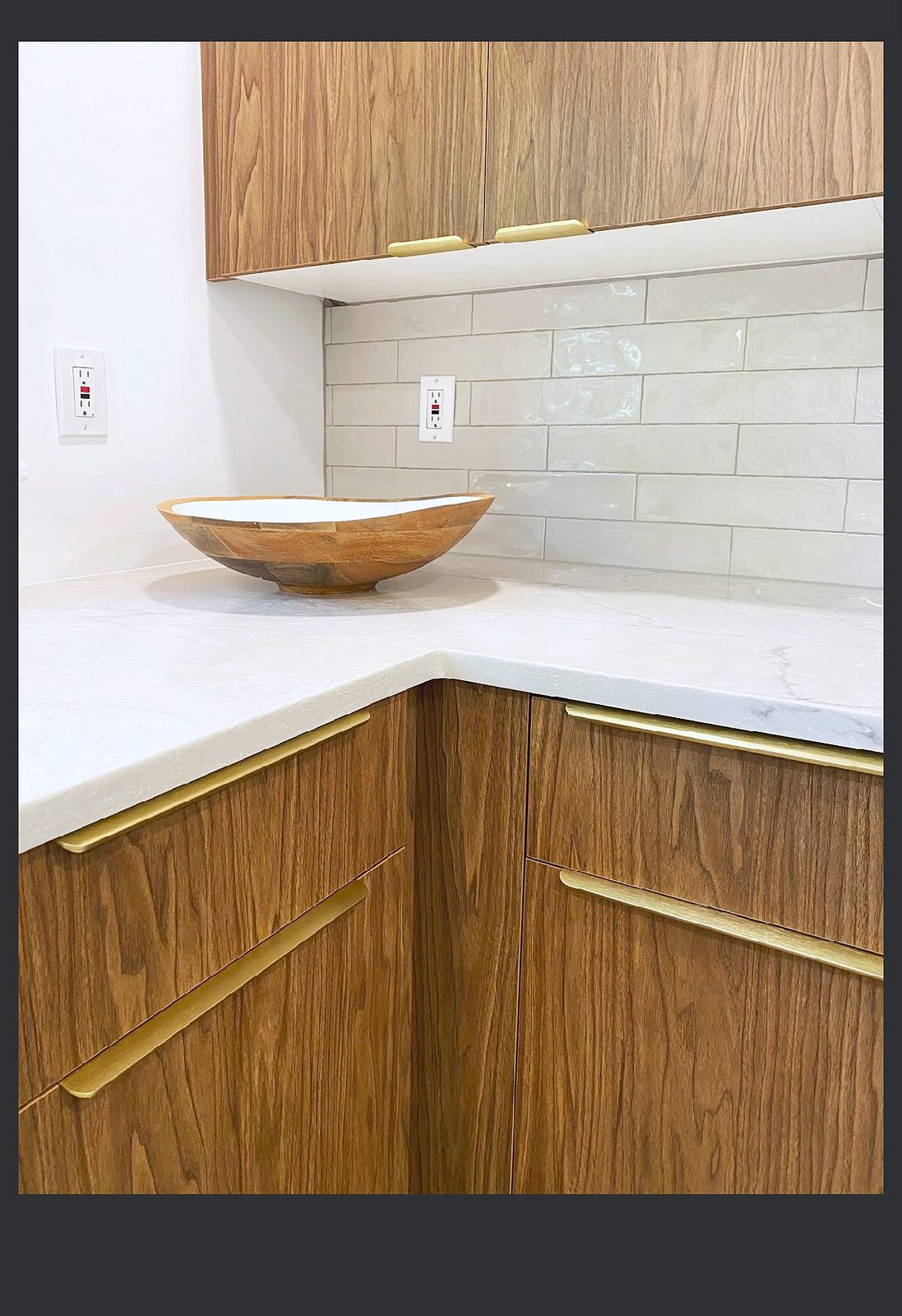 Wine bar with a mirrored backsplash and a dark stone top — Wood-grain slab kitchen with brass pulls and a mirrored wine bar